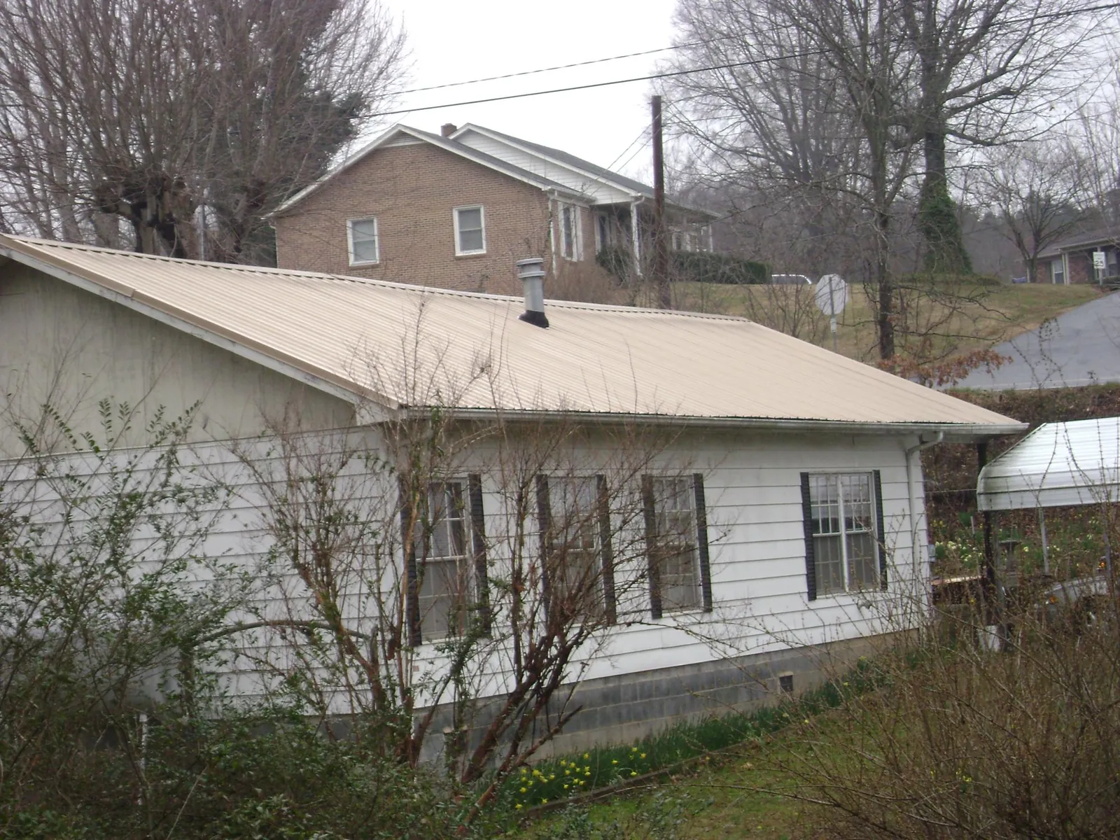 Tan metal roof on a white sided house set into a hillside — Commercial Roofing by Roofing Brothers in Silver Springs